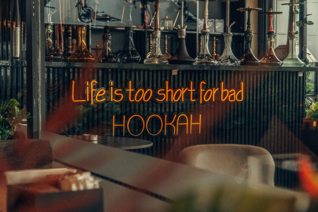 Neon sign reads 'Life is too short for bad HOOKAH' in a chic hookah lounge.