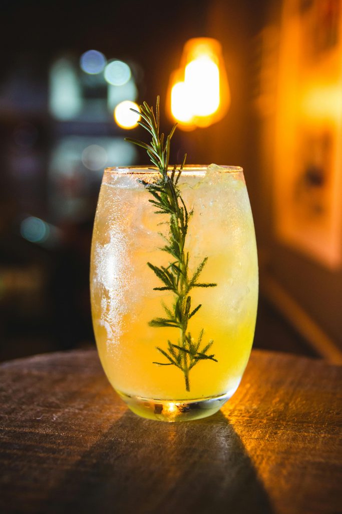 A refreshing cocktail featuring a rosemary garnish served in a glass, perfect for a cozy evening ambiance.